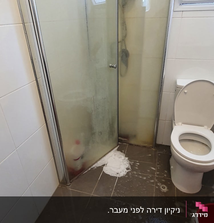 מקלחת עם דלת זכוכית, סבון על הרצפה ודלי אדום